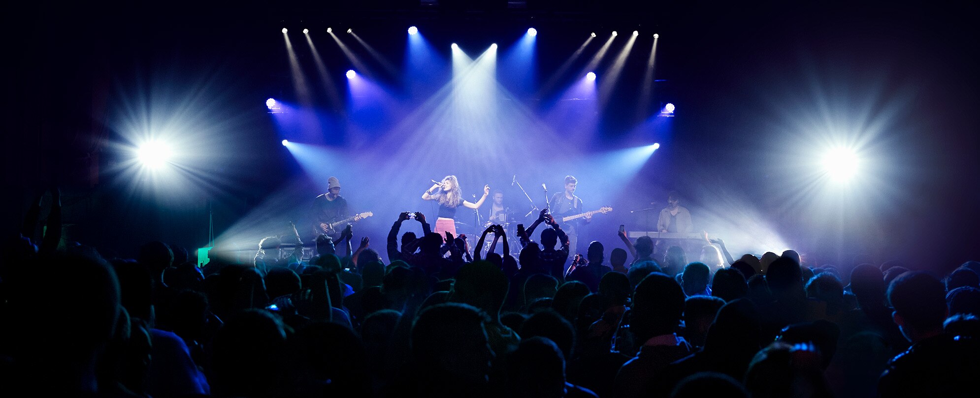 Blue stage lights shine on a female singer with her band performing in front of a crowd in a Las Vegas, Nevada concert.