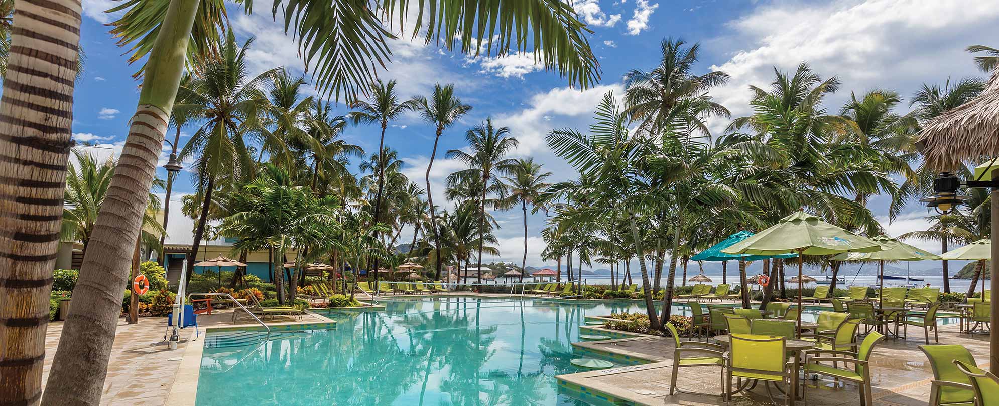 Palm trees and tables with green chairs and umbrellas surround the oceanfront pool at a Margaritaville Vacation Club resort.