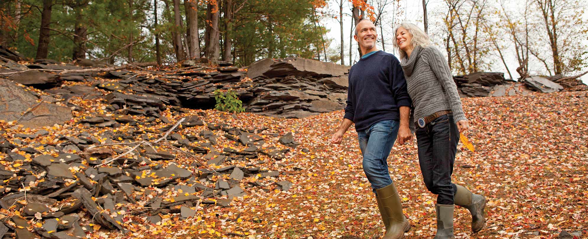 An older couple hikes through forest on an autumn day.