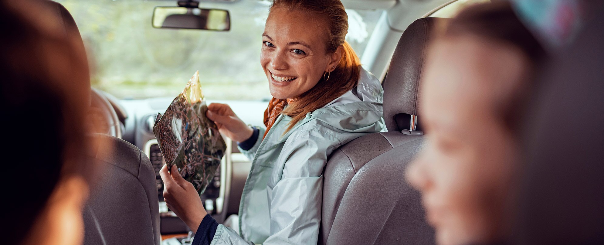 Smiling mom turned around from the front passenger seat of a car, enjoying a family road trip.