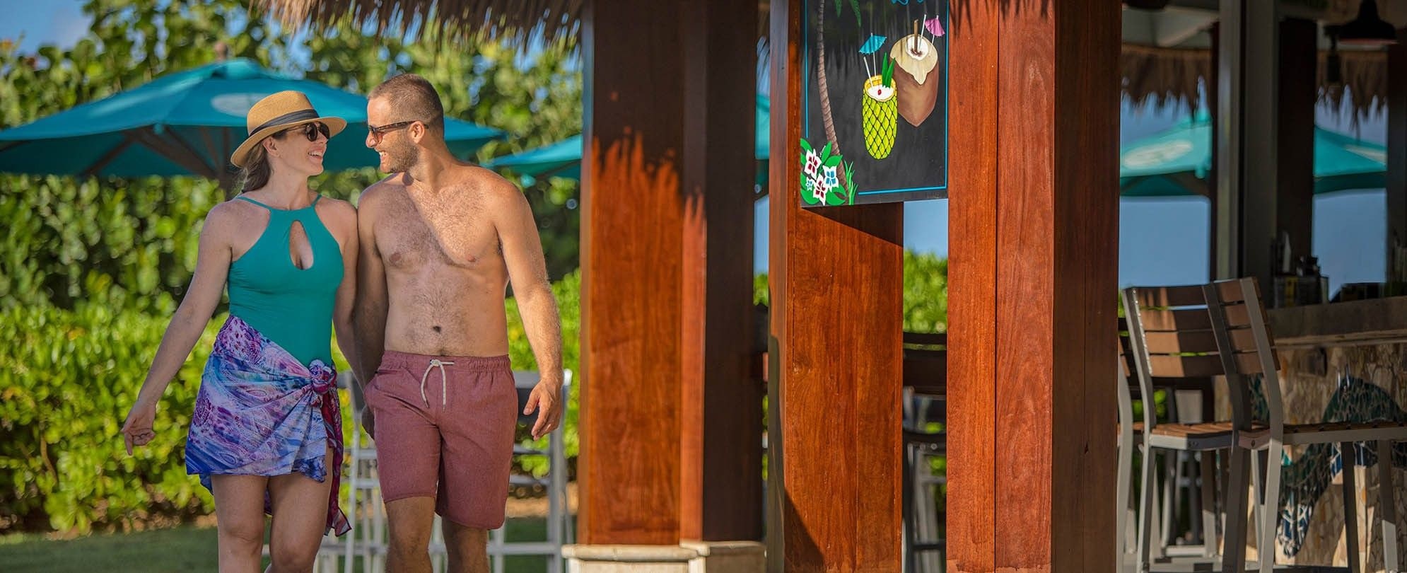 A husband and wife walk together in their bathing suits past the poolside bar at the Margaritaville Vacation Club by Wyndham - Rio Mar resort in Puerto Rico