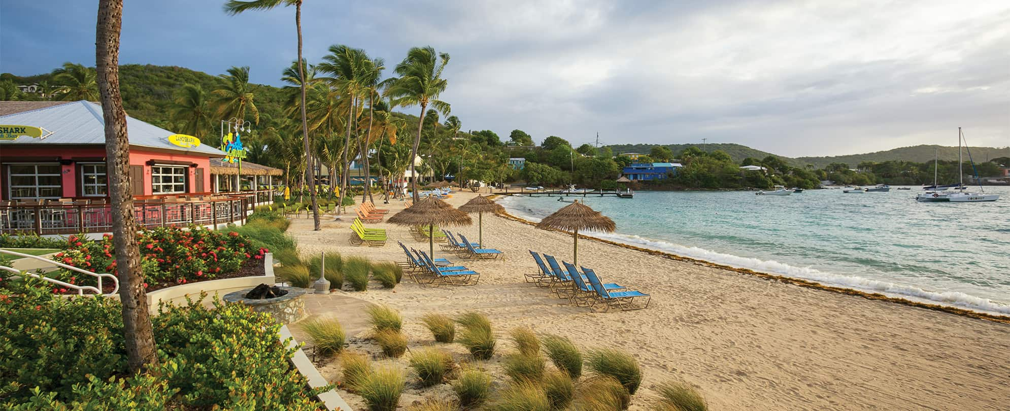 Beach chairs and straw umbrellas by the ocean at Margaritaville Vacation Club by Wyndham - St. Thomas.